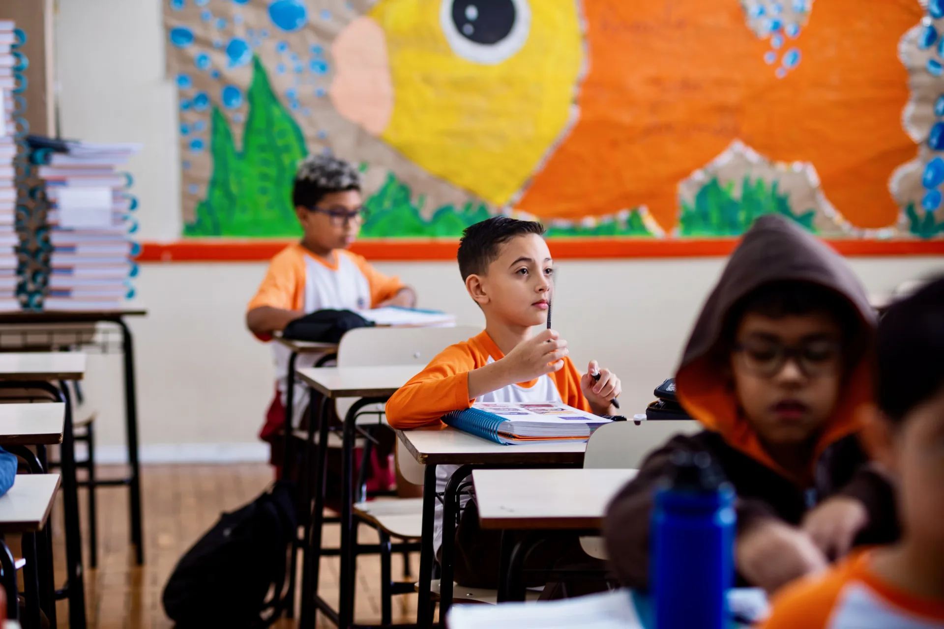 Alunos do Fundamental I em sala, diante do mural da escola