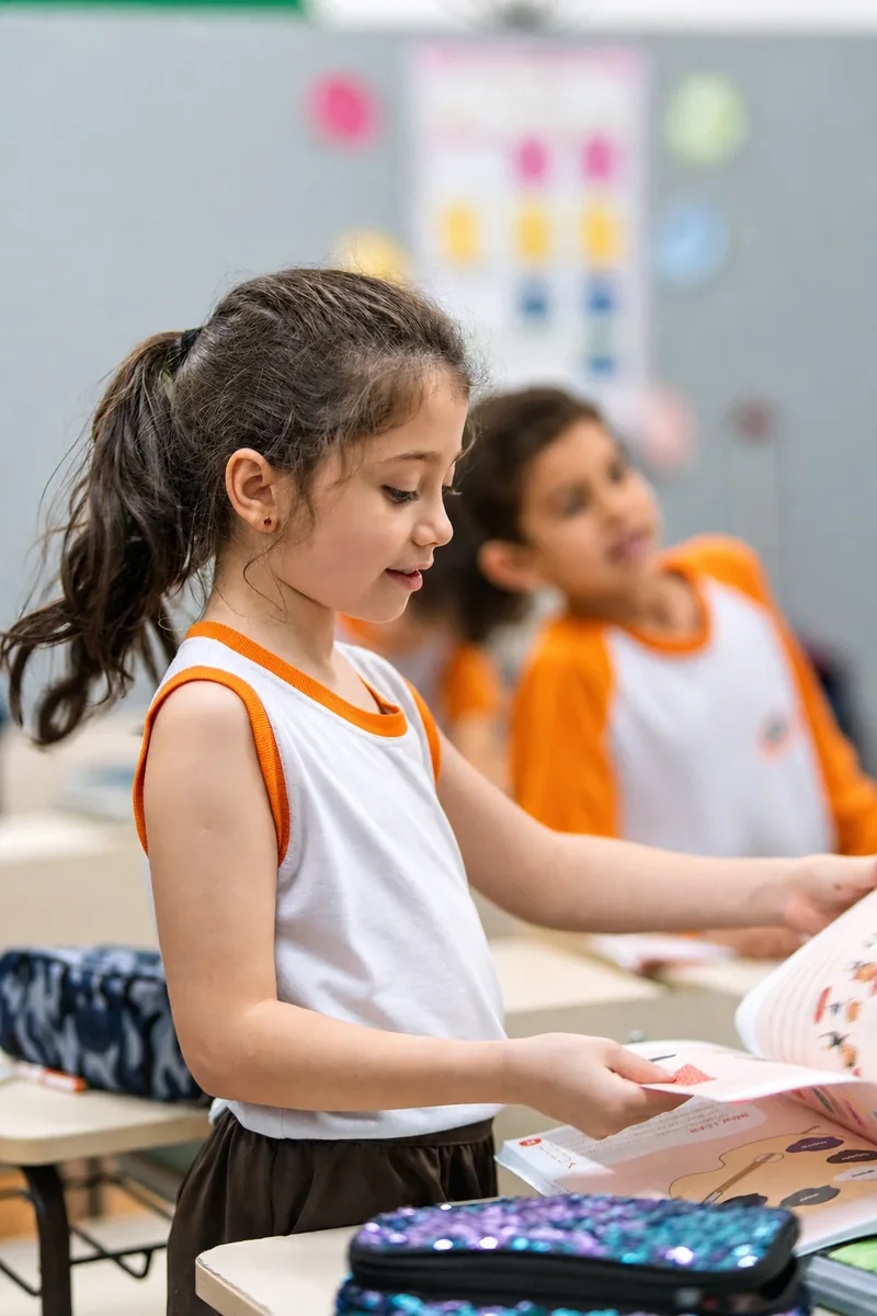 Menina em pé lê o papel colorido que segura sobre o livro aberto da carteira