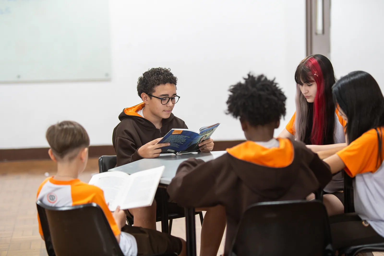 Grupo de alunos lê e conversa em volta da mesma mesa na biblioteca