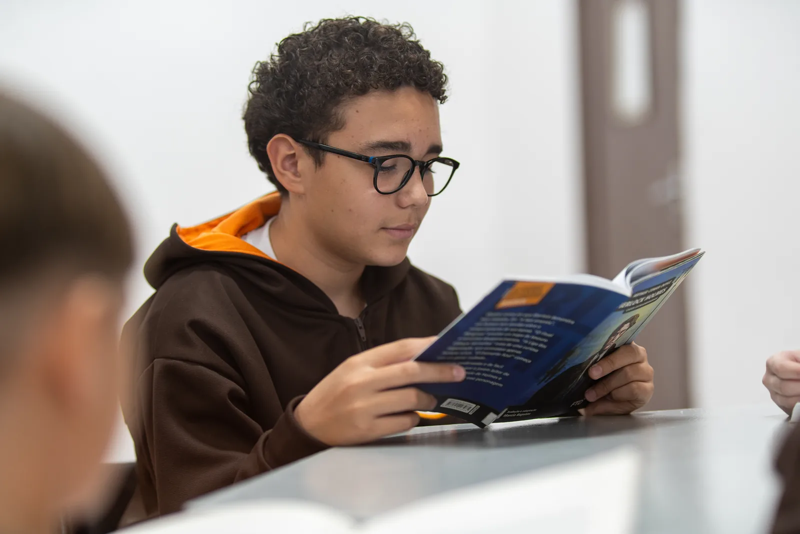 Aluno do Ensino Fundamental II lê um livro apoiado na mesa da biblioteca