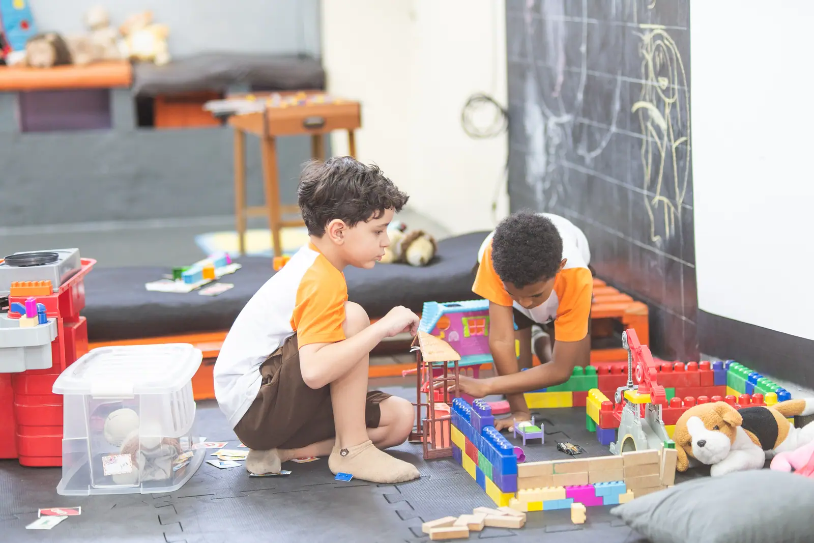 Menino monta uma casinha de brinquedo no tapete da brinquedoteca