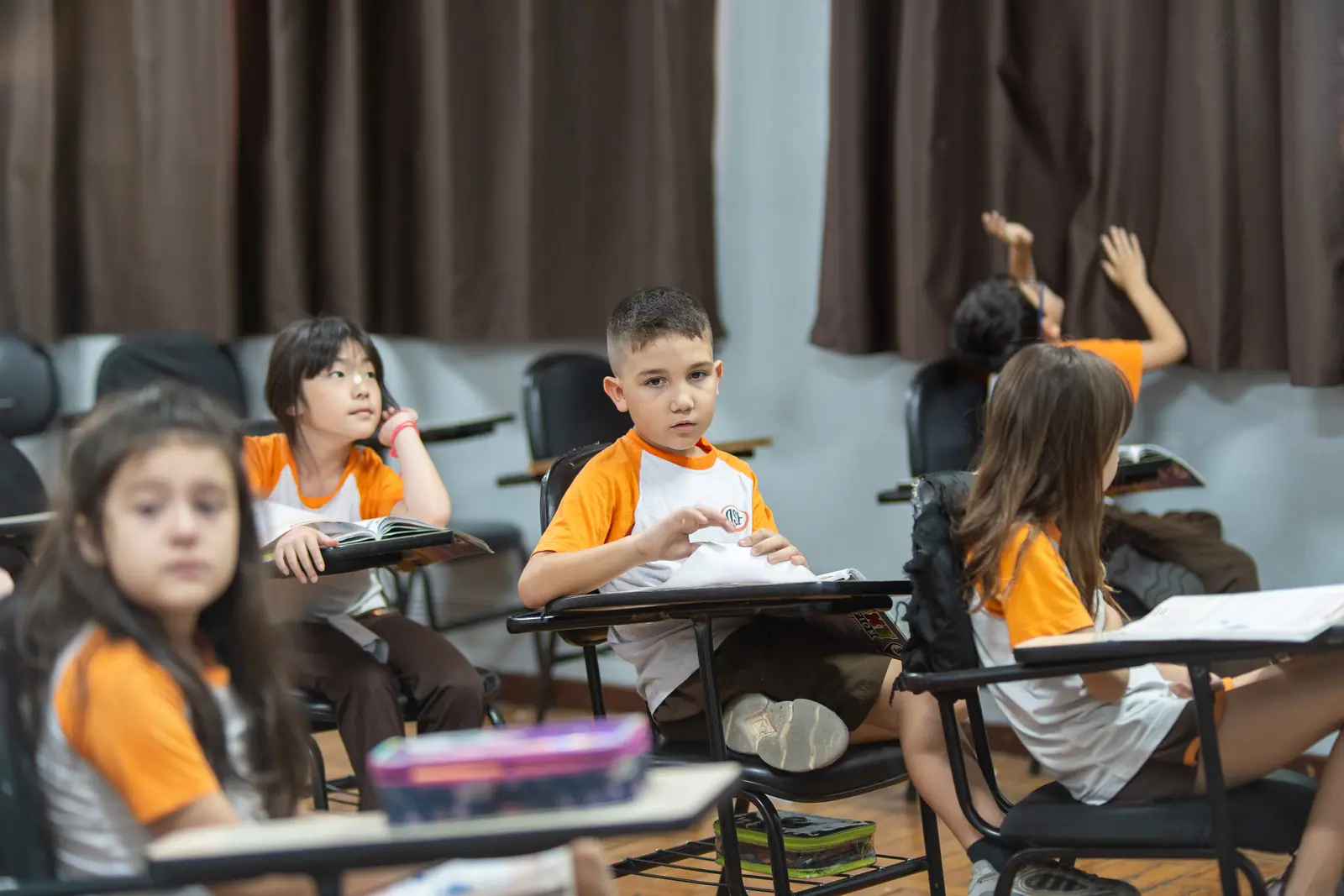 Alunos com o material sobre a prancheta em carteiras espalhadas pela sala