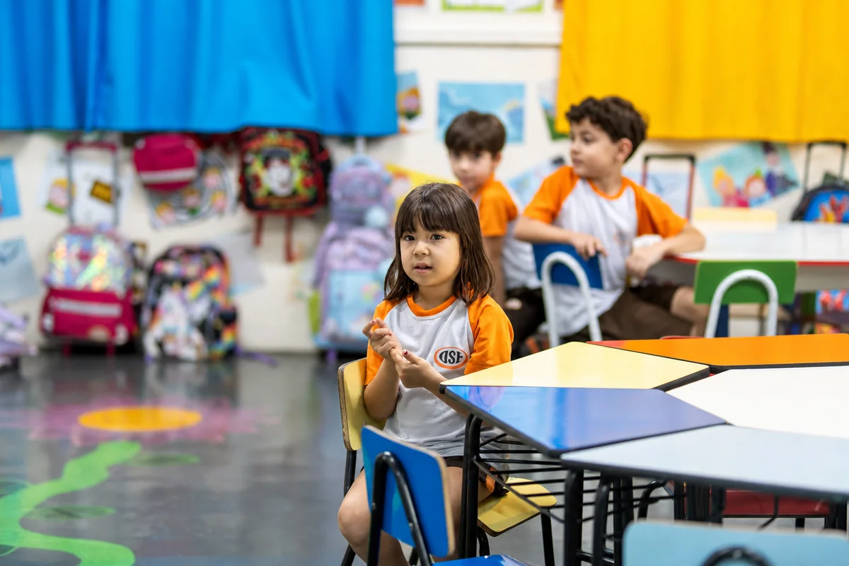 Criança pequena sentada à mesa hexagonal com as mãos juntas