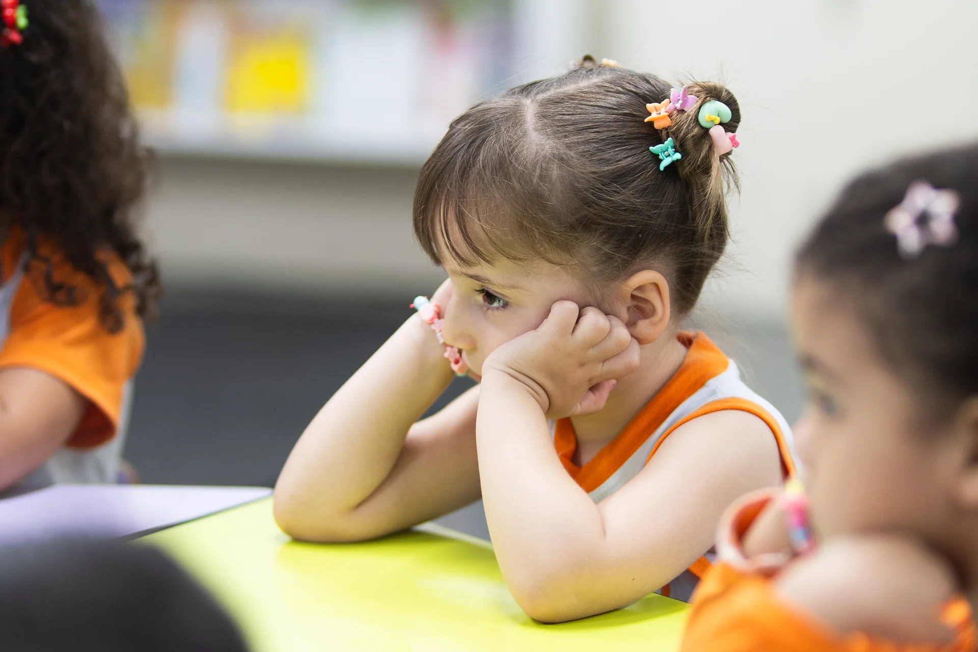 Criança da Educação Infantil apoia o queixo nas mãos sobre a mesa de atividades