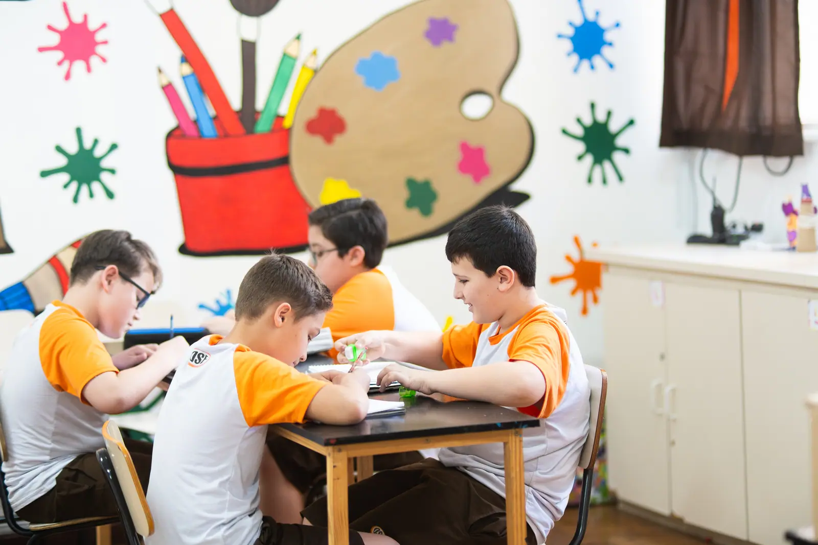 Quatro meninos trabalham em volta da mesa de madeira na sala de arte