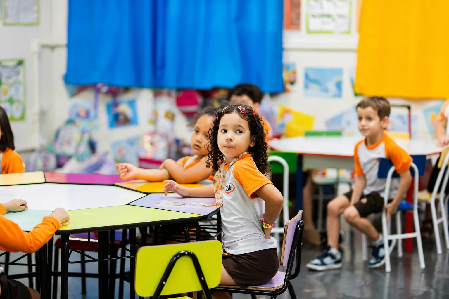 Criança da Educação Infantil trabalha na mesa colorida, com a turma em volta